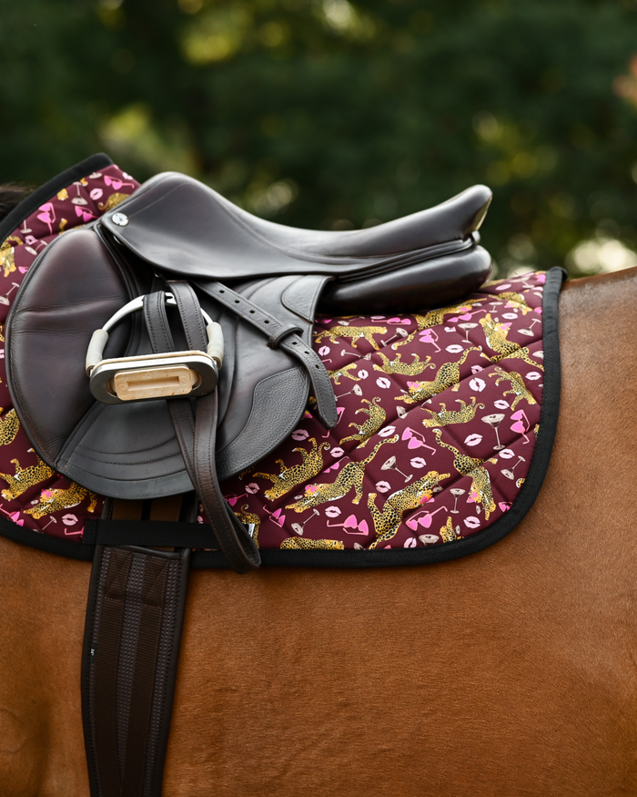 Burgundy Ready to Play pad under a brown close-contact saddle and girth on a bay horse outdoors