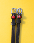 Black leather ManeJane spur straps with red ladybug charms on yellow