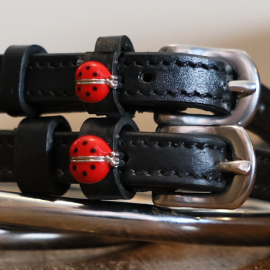 Close-up of red ladybug charms on black leather spur strap keepers