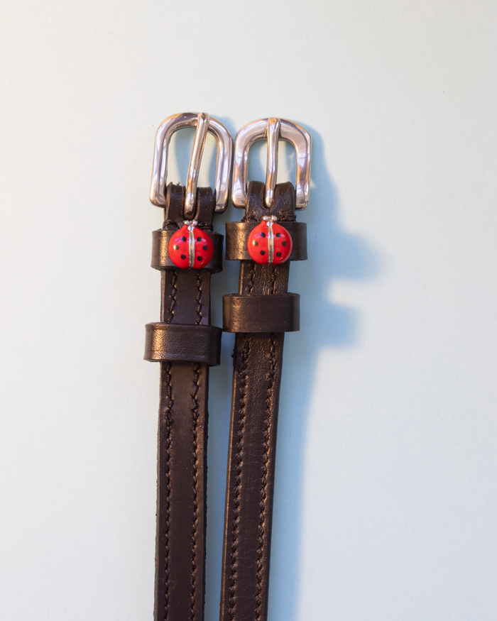 Brown leather ManeJane spur straps with red ladybug charms and silver buckles