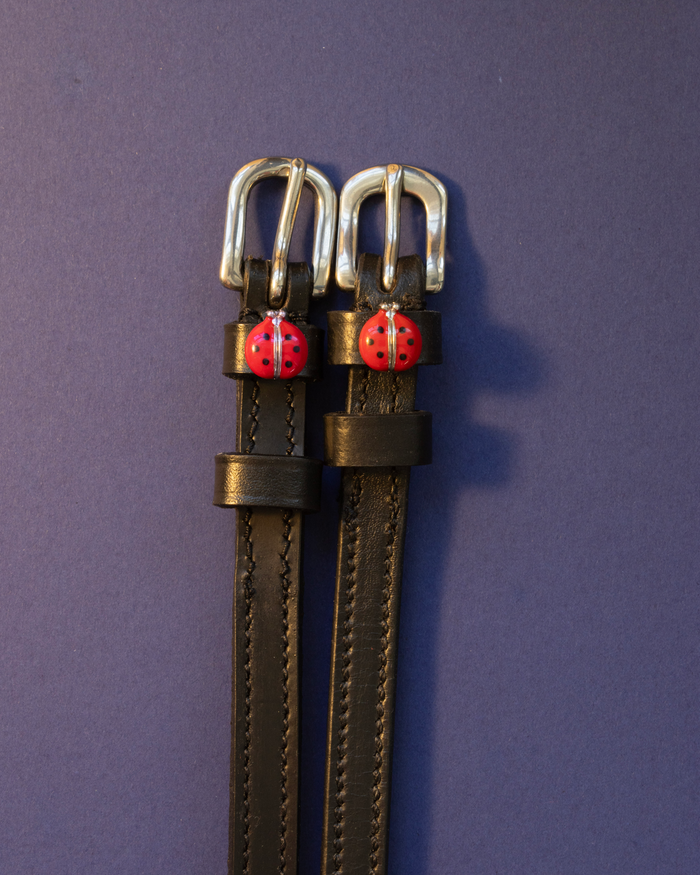 Red ladybug ManeJane spur straps laid flat on a navy background