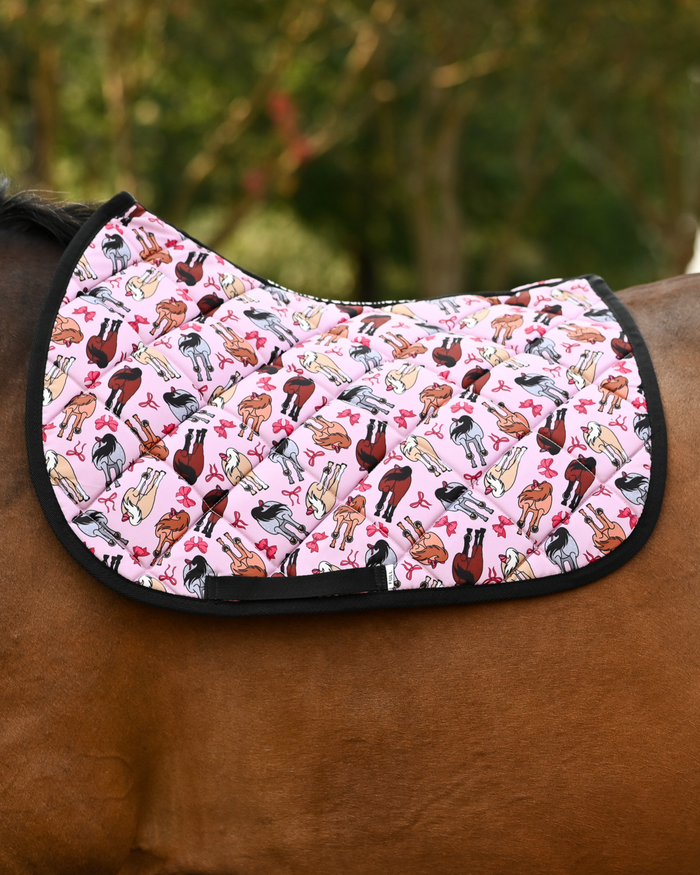 Red Ribbon Girlies saddle pad in light pink, mares with red tail bows, worn unsaddled on a bay horse
