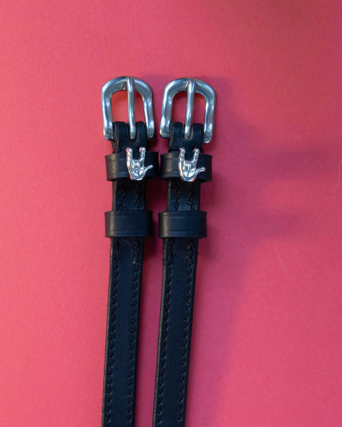 Pair of Rock On ManeJane spur straps, black leather with stainless buckles, on a coral backdrop