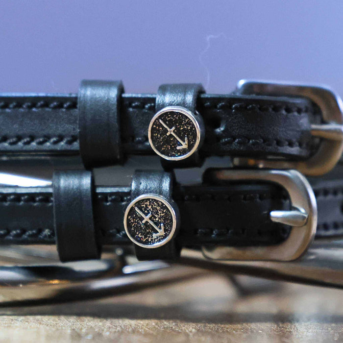 Close-up of Sagittarius arrow zodiac charms on black leather spur strap keepers