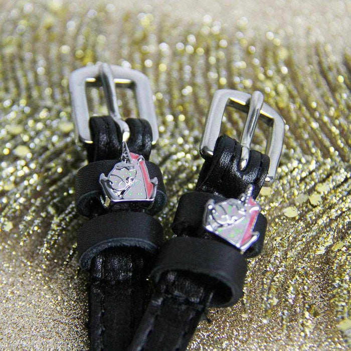 Close-up of silver unicorn charms on black leather spur straps against gold glitter