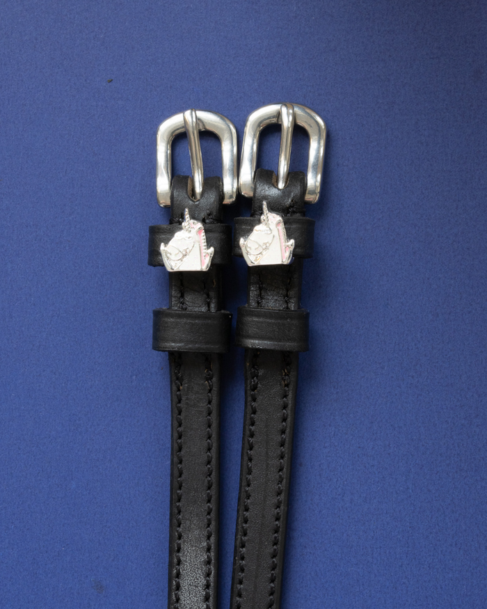 ManeJane unicorn charm spur straps with silver buckles flat-laid on deep blue
