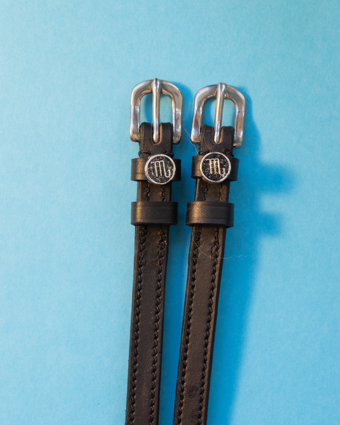 Black leather ManeJane spur straps with silver buckles and round Scorpio zodiac charms on blue