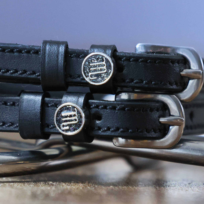 Close-up of silver Scorpio zodiac medallion charms on black leather ManeJane spur straps