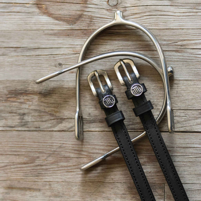 Black leather Scorpio spur straps with a silver spur laid across weathered grey wood