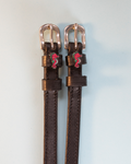 Dark brown leather ManeJane seahorse spur straps with rose-gold buckles, pale blue backdrop