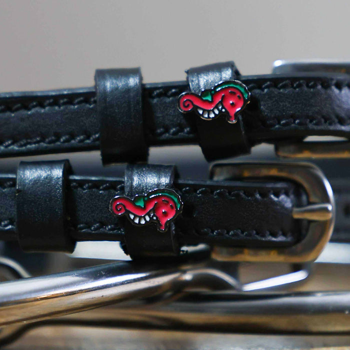 Close-up of pink seahorse charms on black leather spur strap keepers beside a stirrup