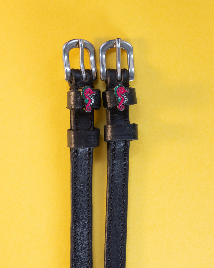 Pair of black leather seahorse spur straps flat-laid on a yellow background