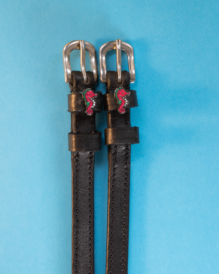 Black leather ManeJane seahorse spur straps on a bright blue background