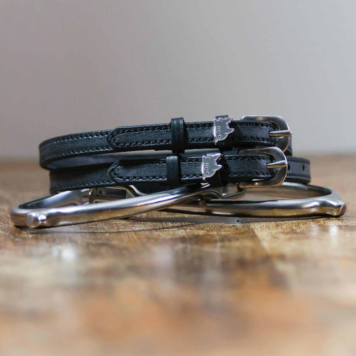 Black shark charm spur straps coiled beside a silver spur on a rustic wood surface