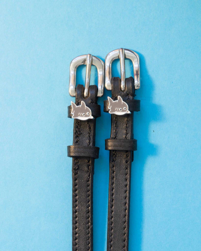 Black leather shark charm spur straps with silver buckles on a light blue background