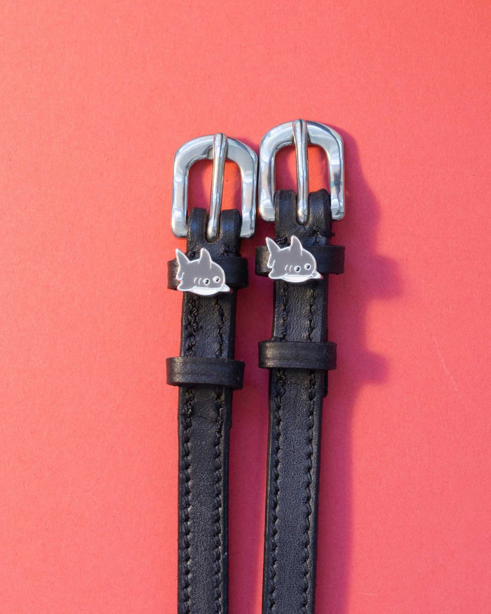 Silver shark charm spur straps on black leather over a coral red background