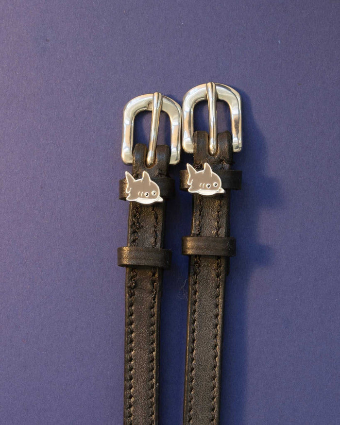 Silver shark charm spur straps on black leather against a deep purple background