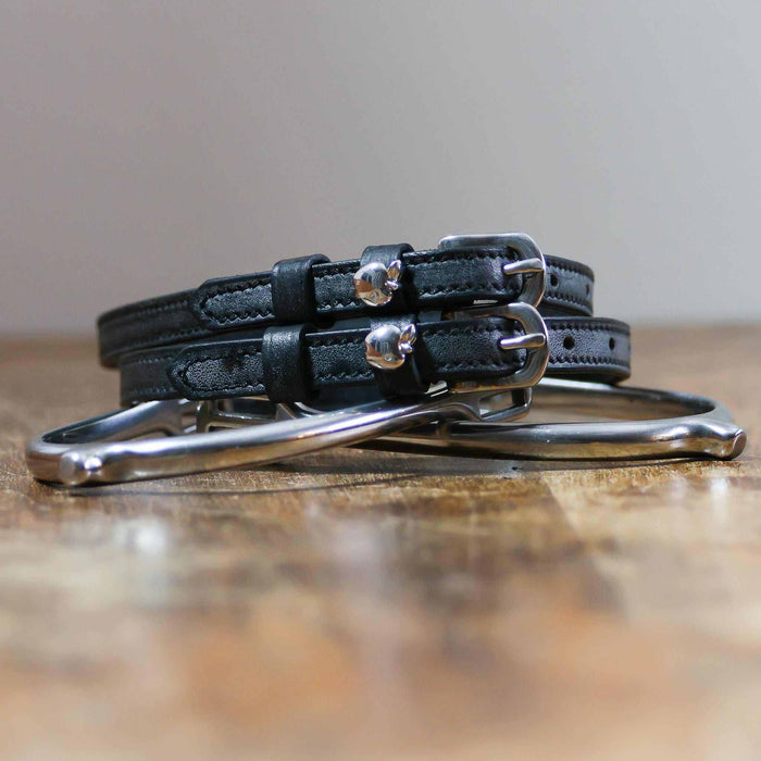 Silver apple spur straps coiled on a stirrup on a wooden table