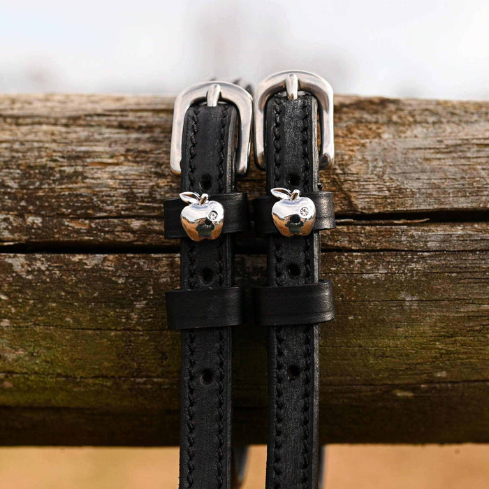Black leather silver-apple spur straps with buckles draped over a weathered wood rail