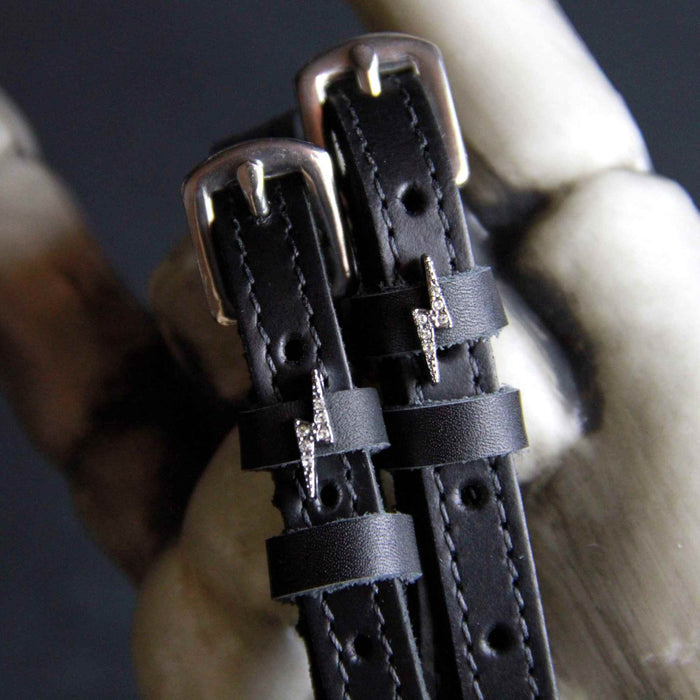 Close-up of rhinestone bolt charm spur straps resting against a pale bone prop
