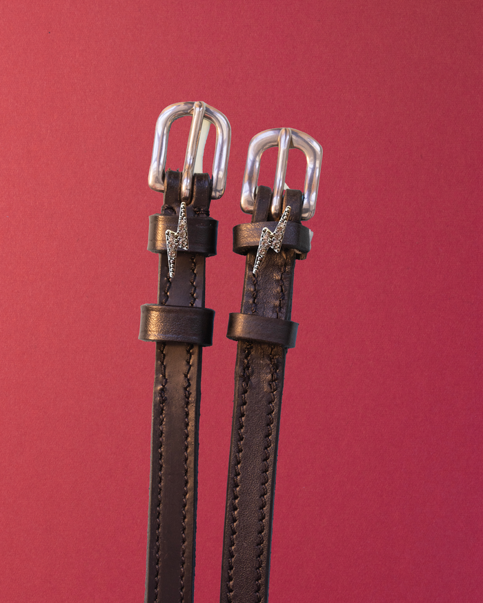 Brown leather lightning bolt spur straps with silver buckles on deep burgundy