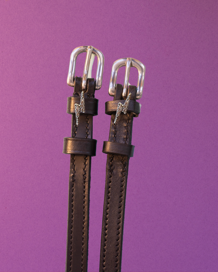 Rhinestone lightning bolt spur straps on brown leather against a purple background