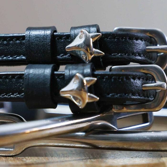 Close-up of silver fox head charms on the keepers of black leather spur straps