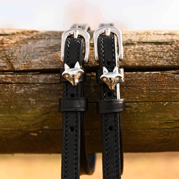 Black leather silver fox spur straps hanging over a weathered wooden fence rail