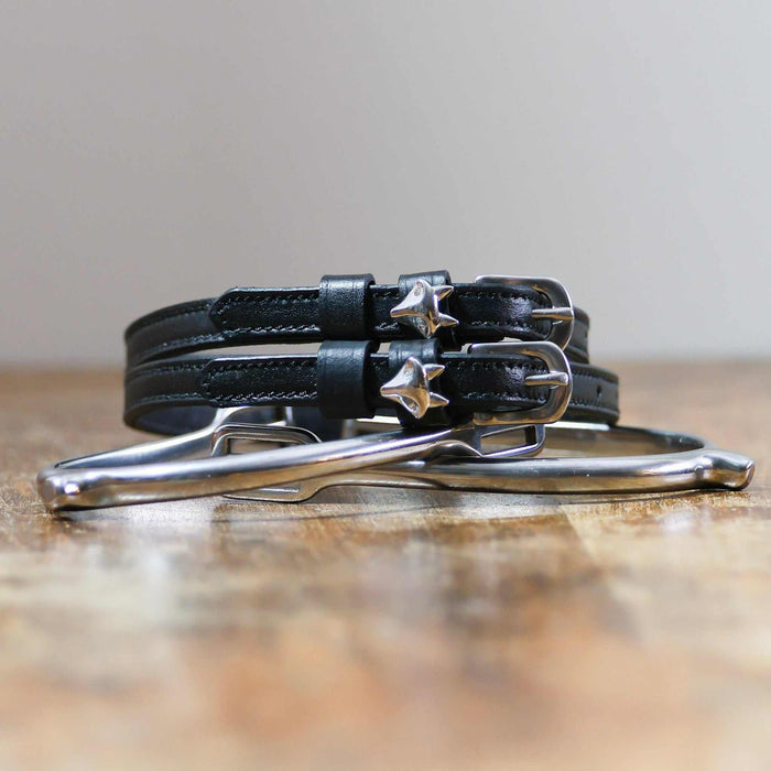 Coiled black leather ManeJane silver fox spur straps stacked on a spur on a wooden table
