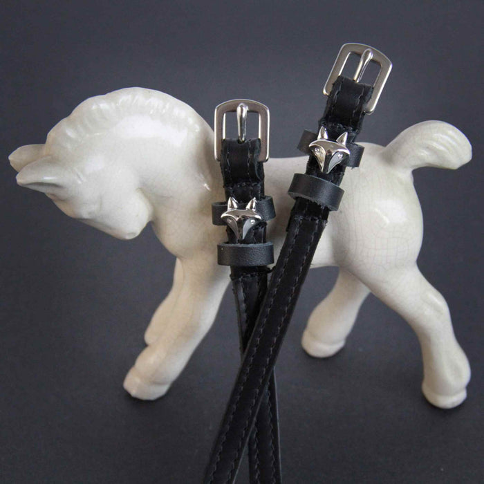 Black leather silver fox spur straps draped over a white ceramic foal figurine