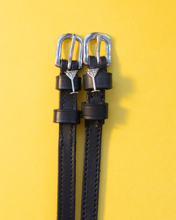 Pair of black leather martini glass spur straps laid flat on a yellow background