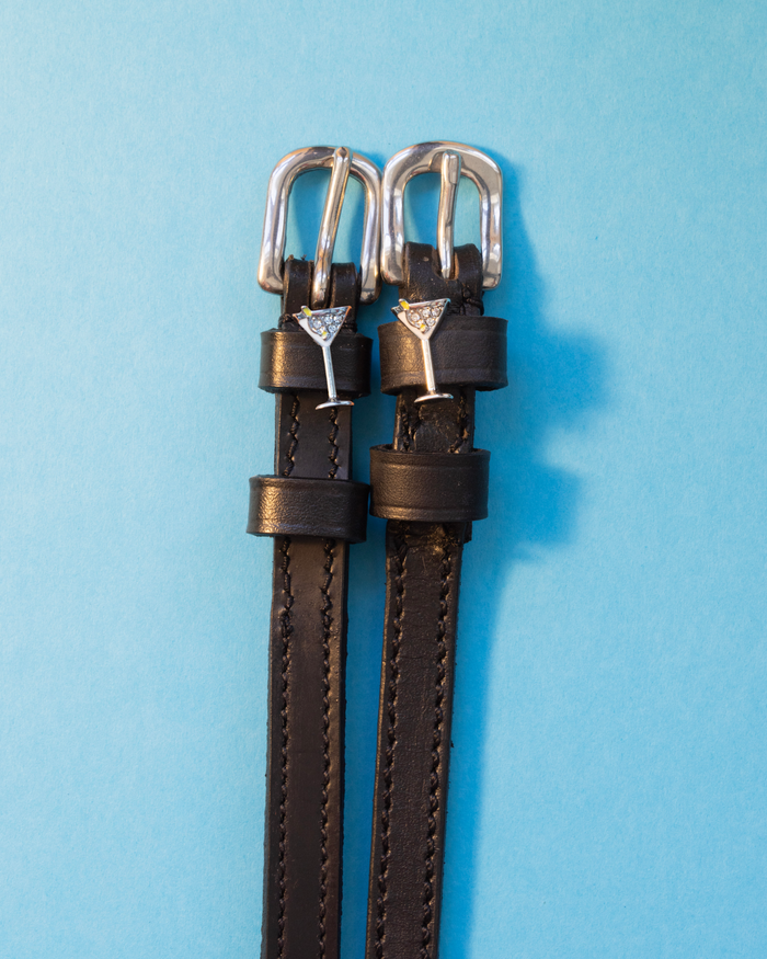 Black leather martini glass spur straps with silver buckles on a light blue background