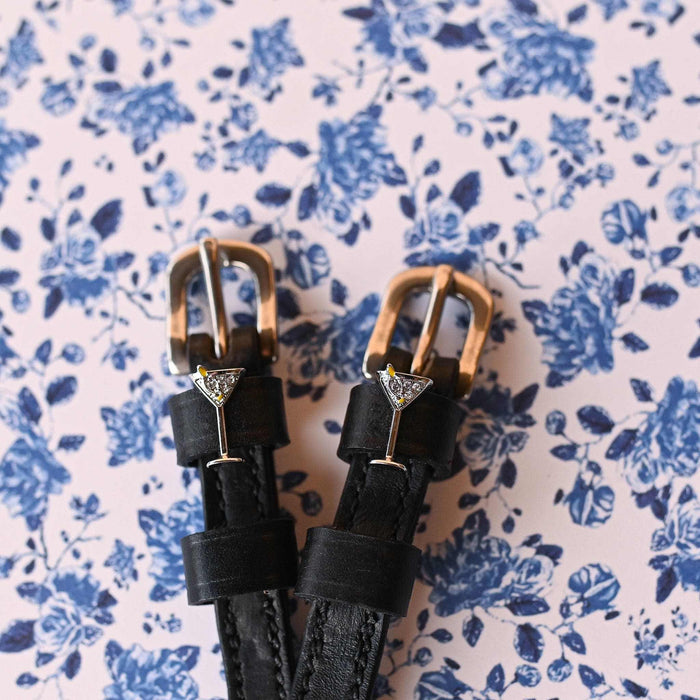 Martini glass ManeJane spur straps with brass buckles on blue floral wallpaper