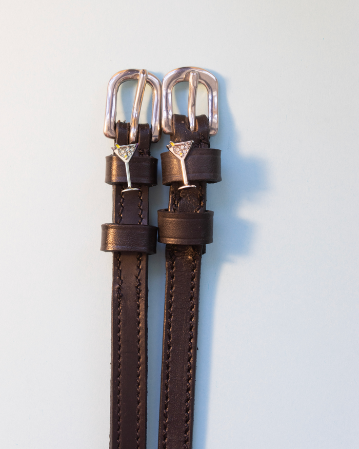 Dark brown leather martini glass spur straps with silver buckles on off-white