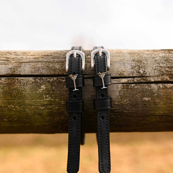 ManeJane martini glass spur straps hanging over a weathered wooden fence rail