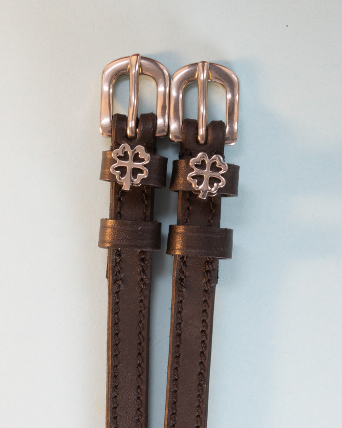 Brown leather ManeJane spur straps with rose-gold buckles and silver openwork clover charms