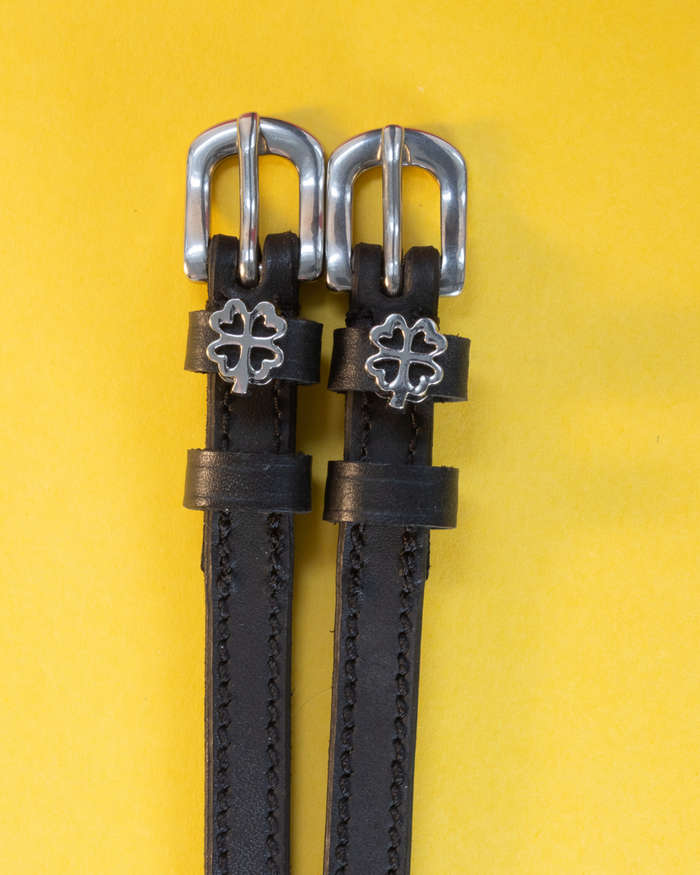 Silver openwork clover charms on black leather ManeJane spur straps, yellow background