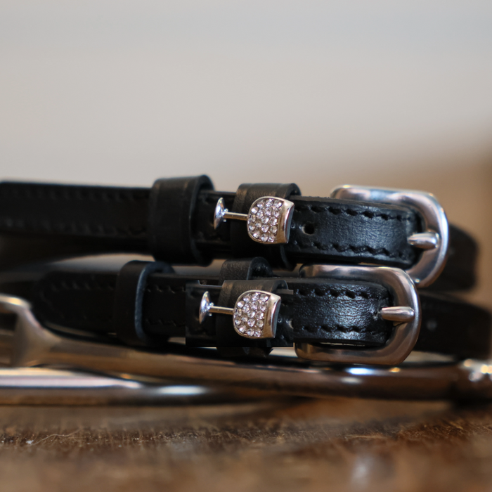 Black leather wine glass spur straps coiled beside a silver spur on a wooden surface