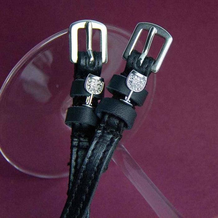 Close-up of crystal wine glass charms on black leather spur straps on burgundy