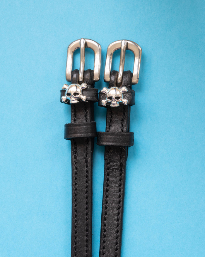 Pair of black leather skull and crossbones spur straps with silver buckles on bright blue