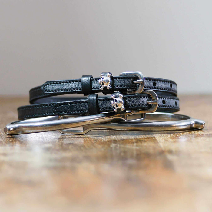 Black leather skull and crossbones spur straps coiled beside a silver spur on wood