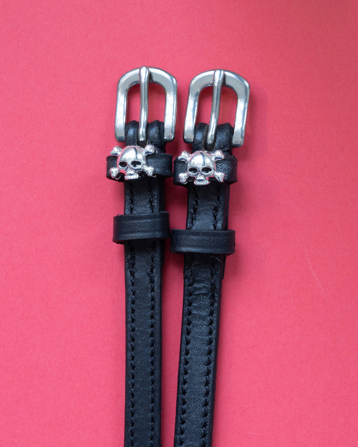 Black leather skull and crossbones spur straps with silver buckles on coral red