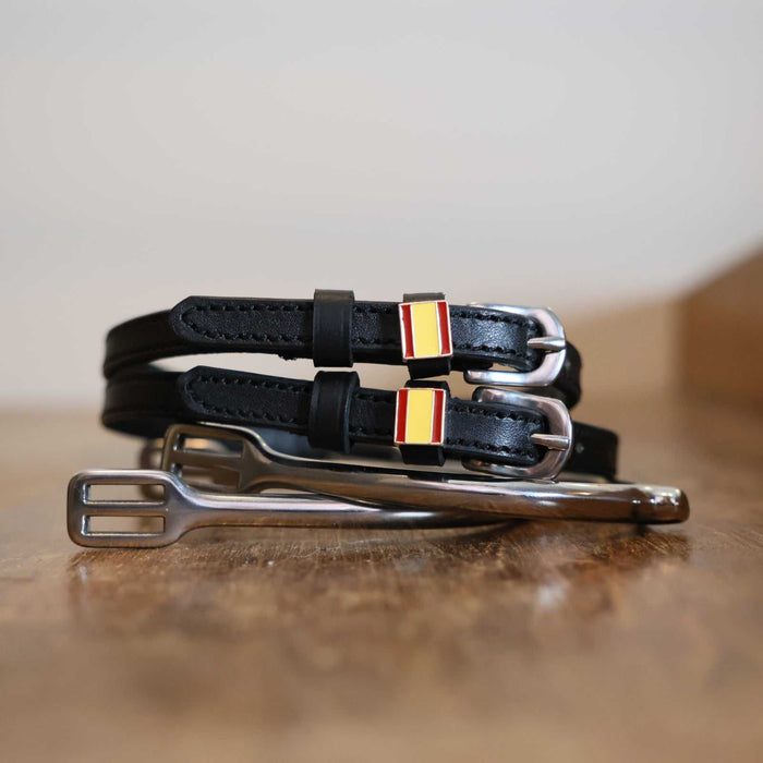 Spanish flag charm spur straps coiled beside a stirrup on a wooden tabletop