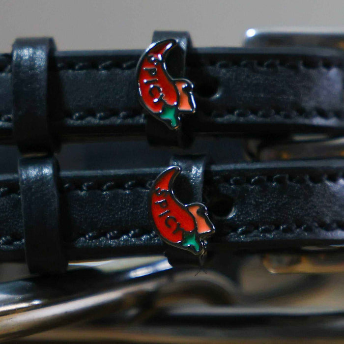 Close-up of red chili pepper charms on black leather ManeJane spur straps, silver spur behind