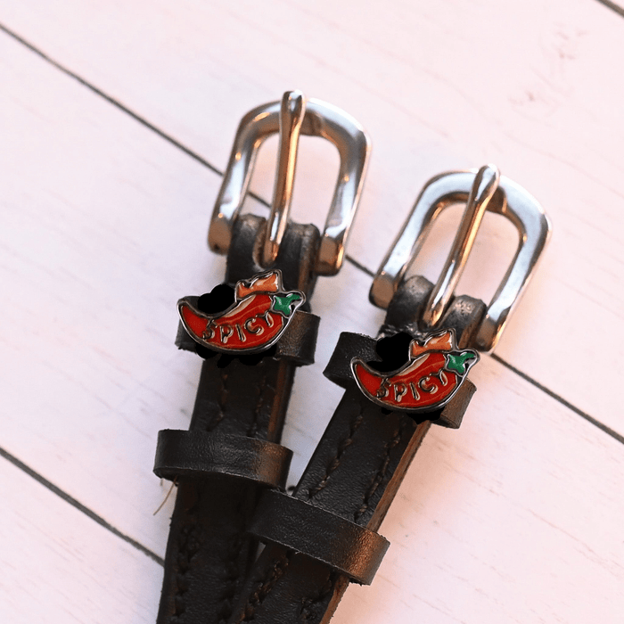 Angled close-up of red 'SPICY' chili charms on black leather ManeJane spur straps