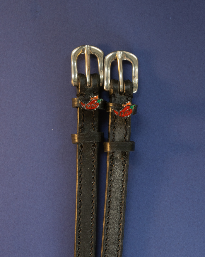Black leather chili pepper ManeJane spur straps with silver buckles on a navy background
