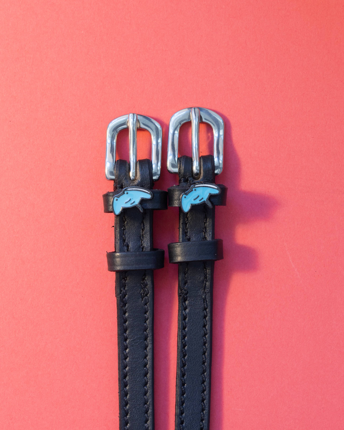 Black leather stingray spur straps with blue ray charms on a coral background, ManeJane