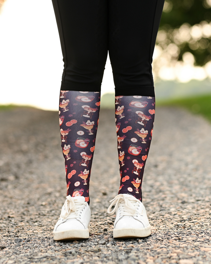 Stir Crazy riding boot socks styled over breeches, dark plum with cocktail glasses and citrus slices