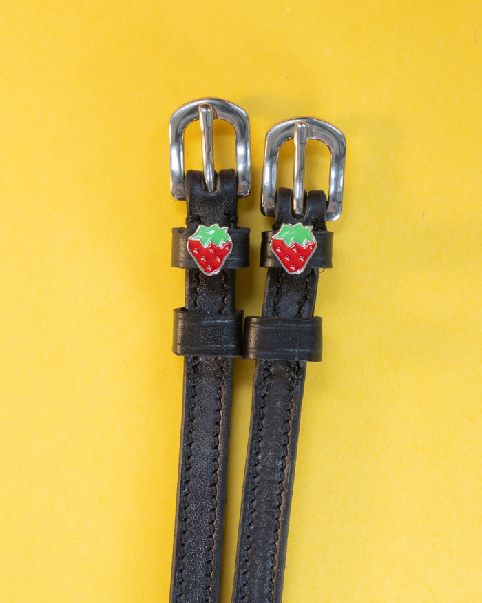 Black leather strawberry spur straps with red strawberry charms on a yellow background