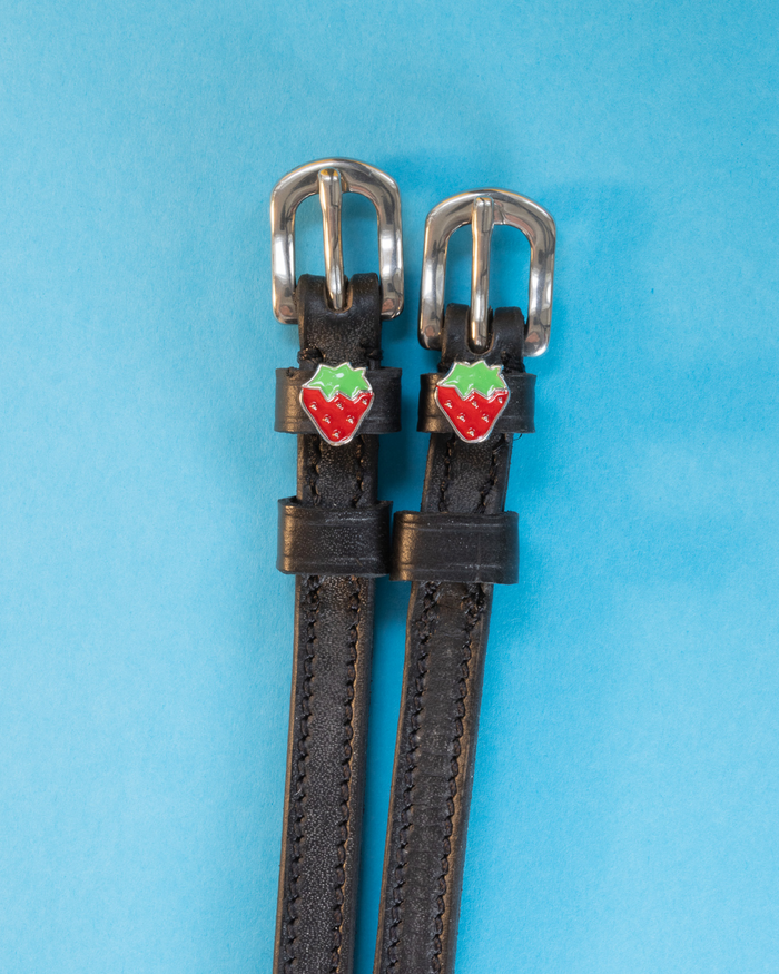 Black leather strawberry spur straps with enamel strawberry charms on a light blue background